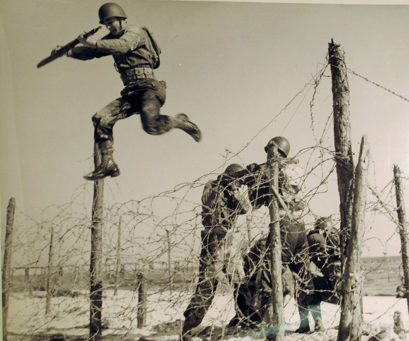 Image of old war photo of military men jumping barbwire in Camp Gordon Johnston.