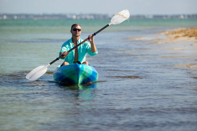 Image of a man paddling his kayak along the shoreline.