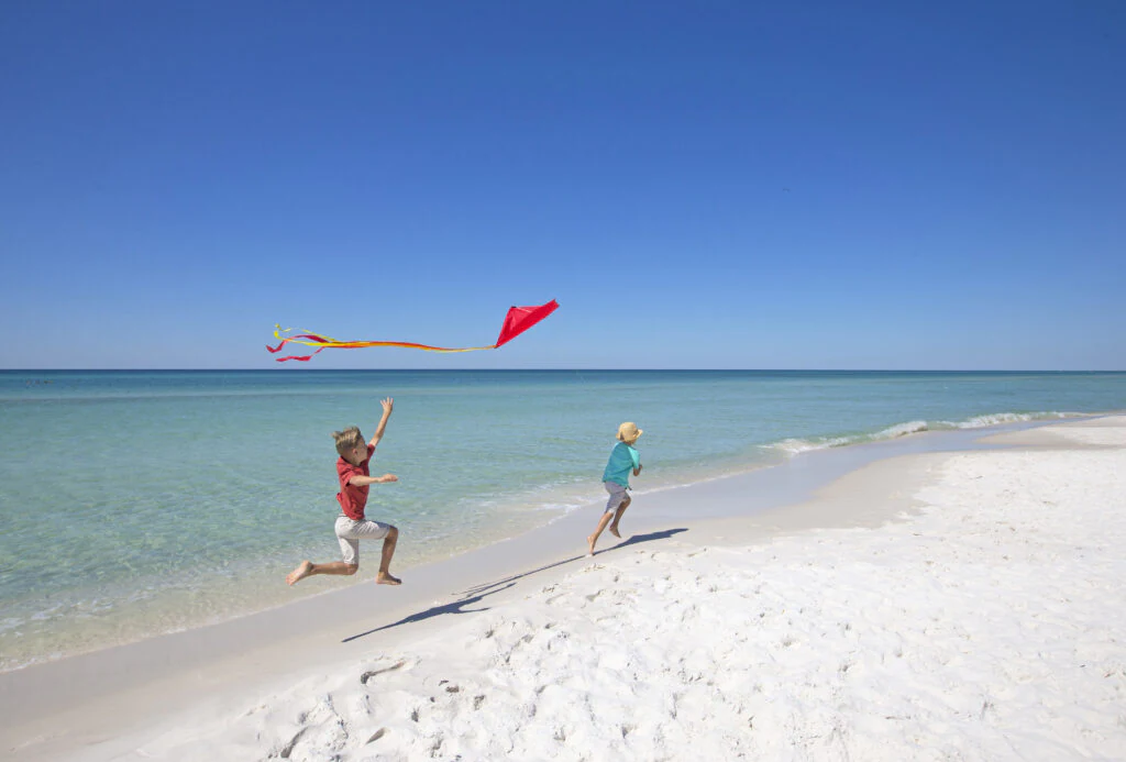 Image of two kids running on the beach with kites.